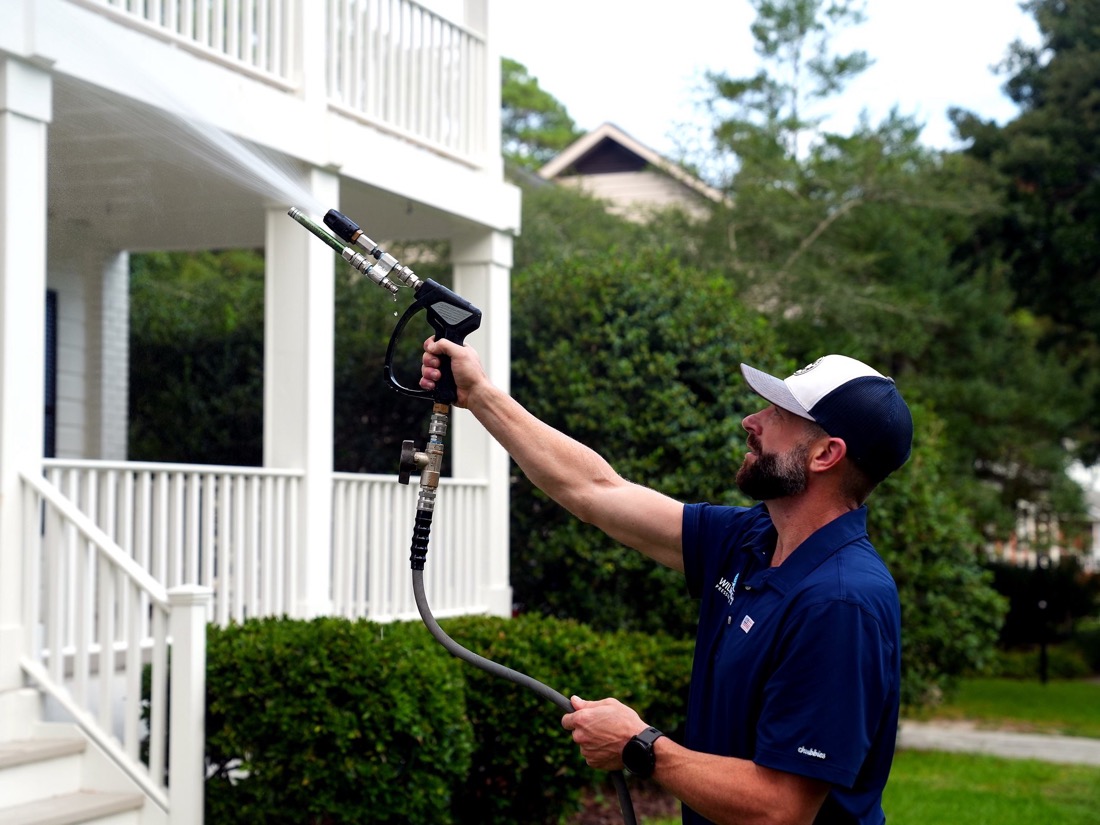 Cameron soft washing the white porch columns of a Wilmington NC home, low-pressure spray fanning across the trim