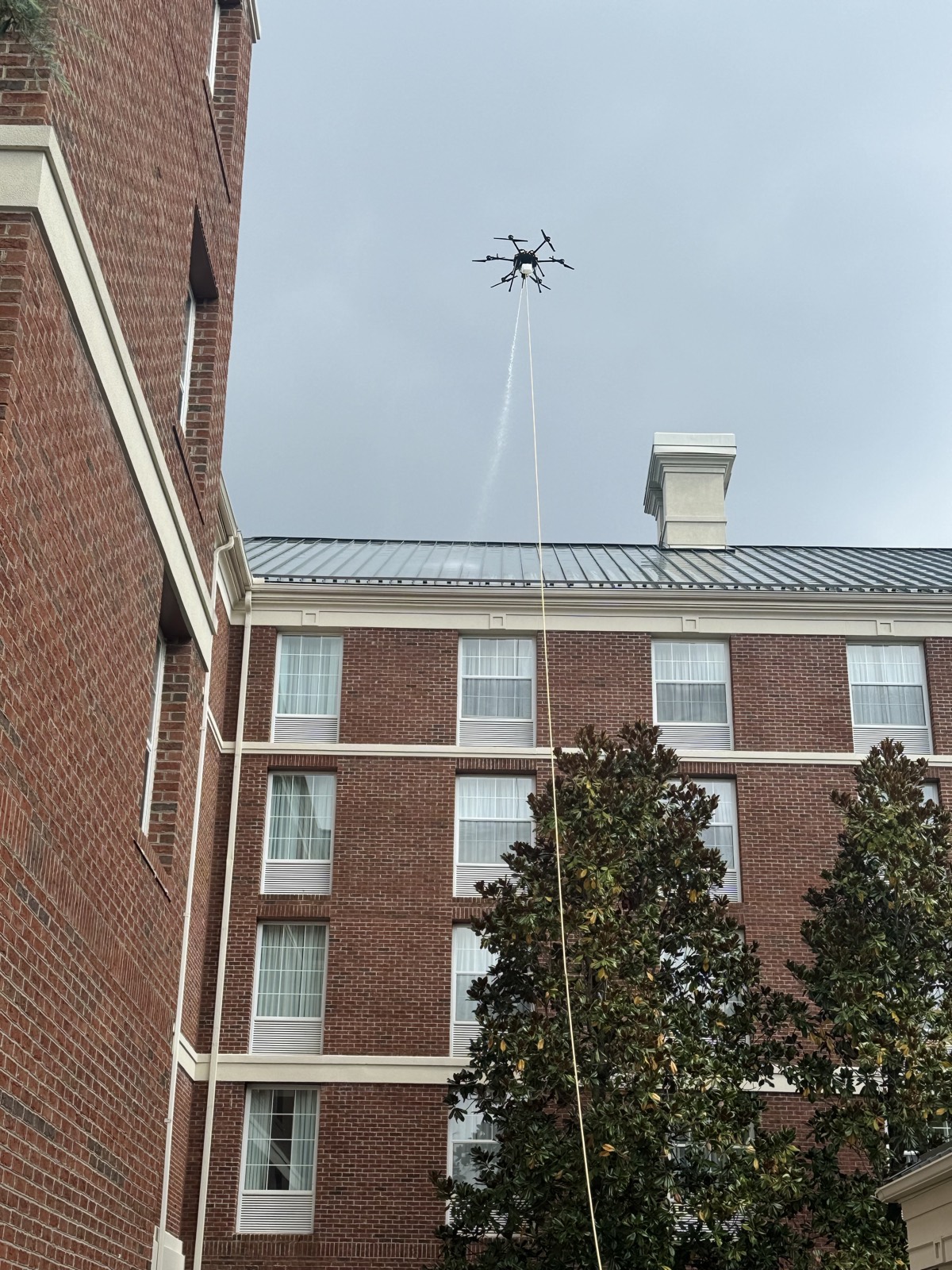 Cleaning drone washing the metal roof and upper brick wall of a multi-story building