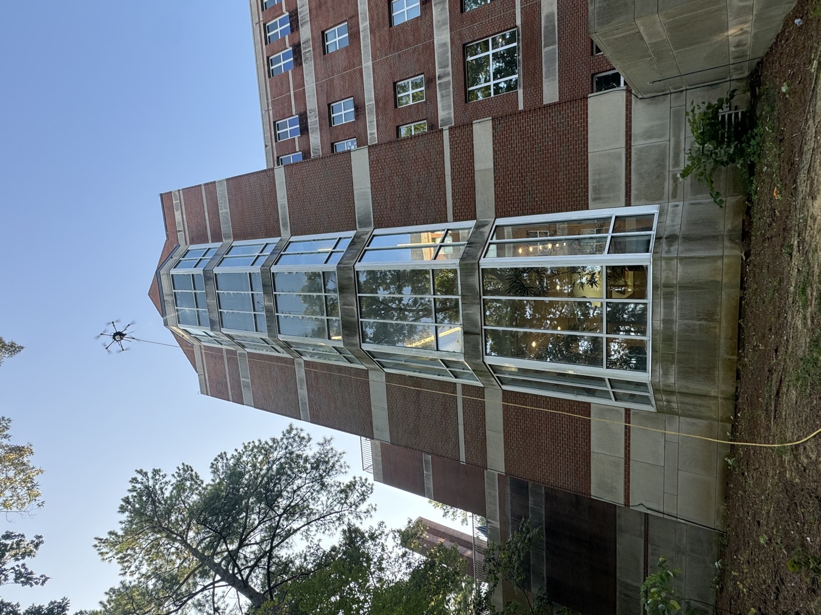 Cleaning drone at the top of a tall glass stairwell tower on a brick building