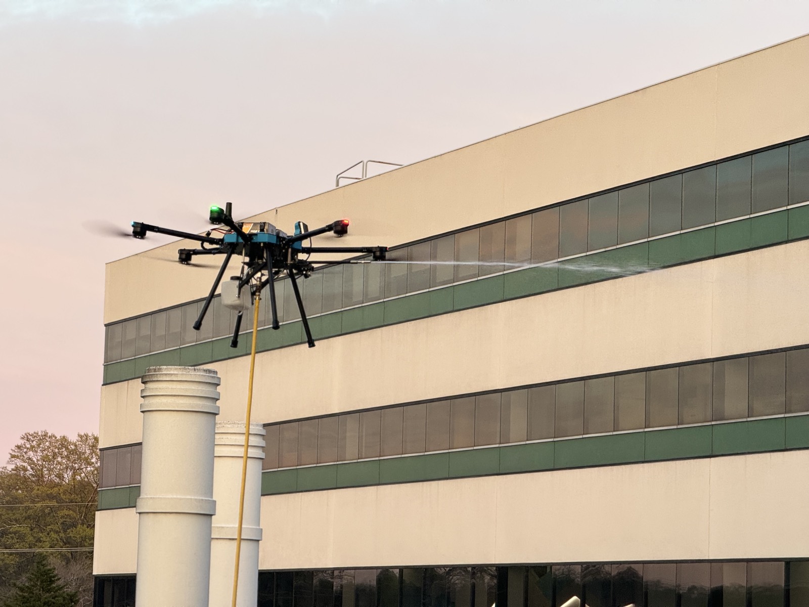 Cleaning drone spraying the upper wall of a multi-story office building at dusk