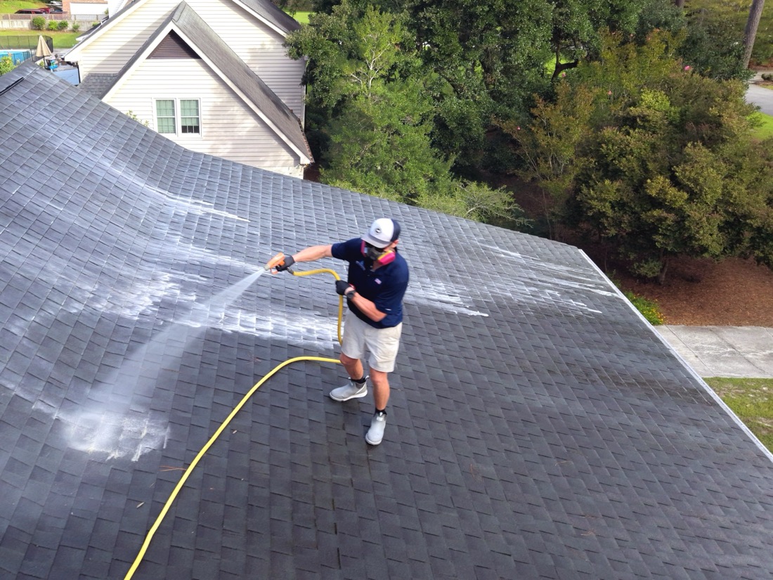Asphalt shingle roof being soft washed in Wilmington NC, seen from above — clean stripes beside algae-stained shingles
