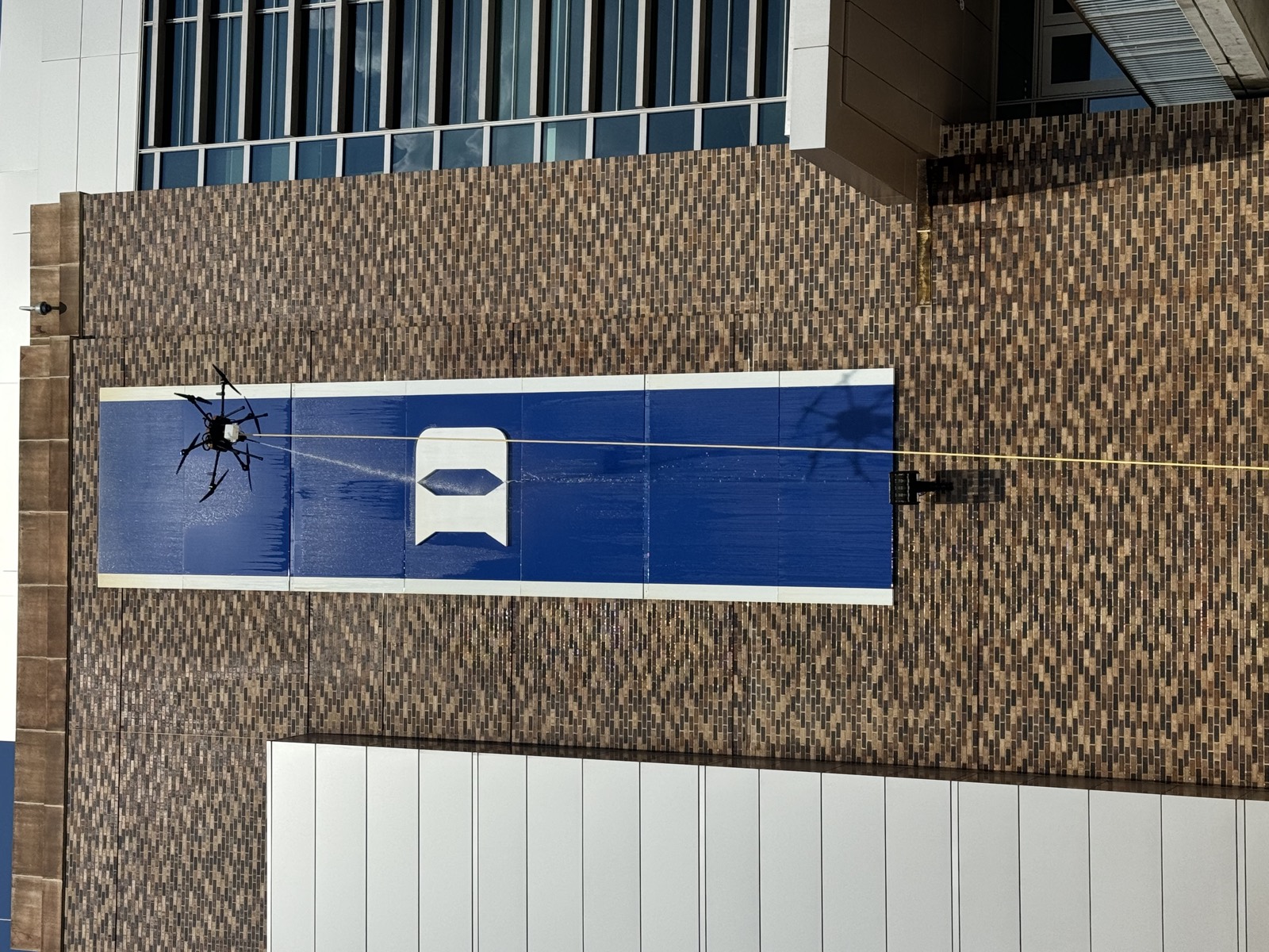 Cleaning drone washing a tall banner on a brick stadium wall