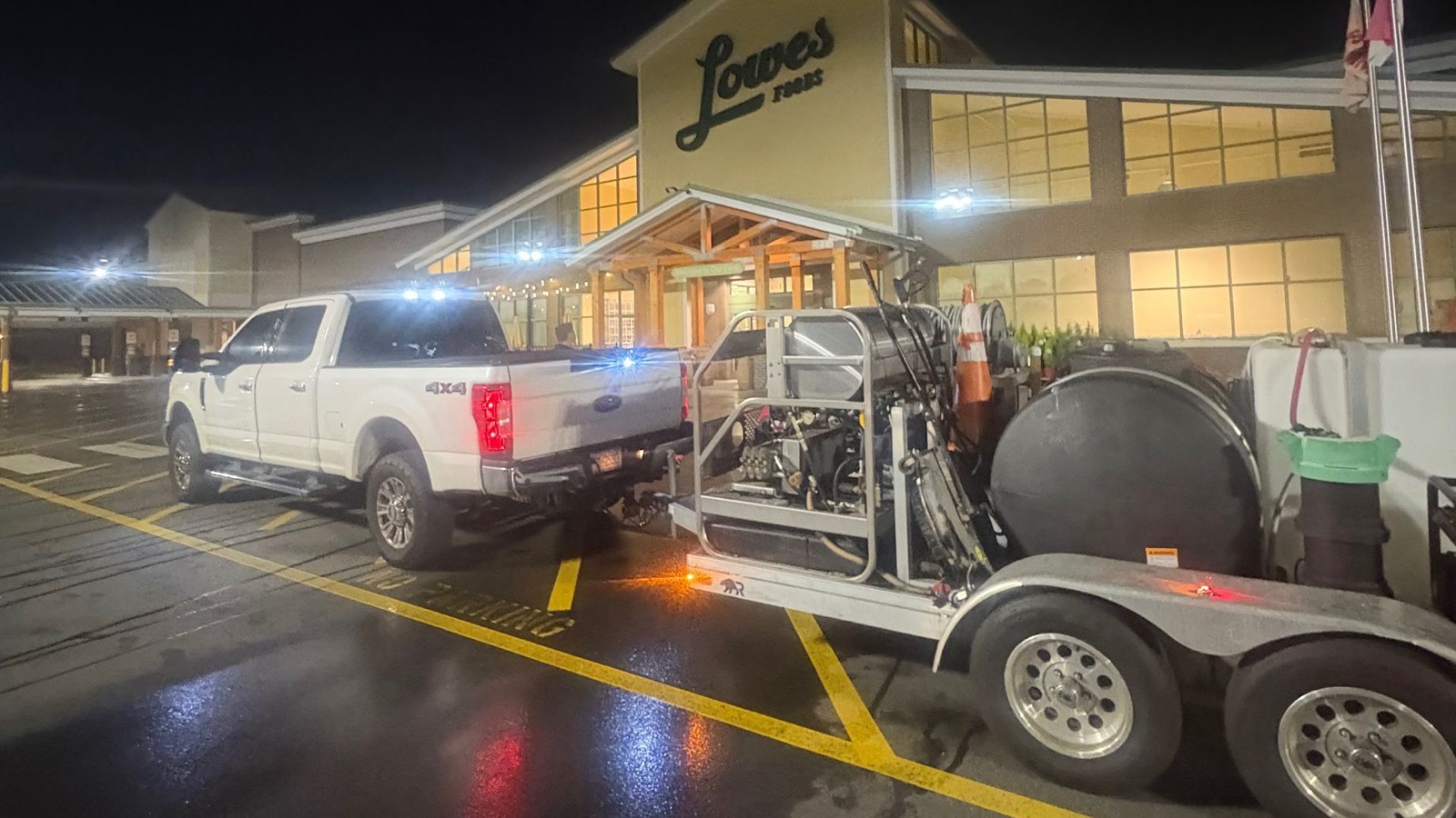 Pickup truck and pressure-washing trailer rig outside a grocery store at night