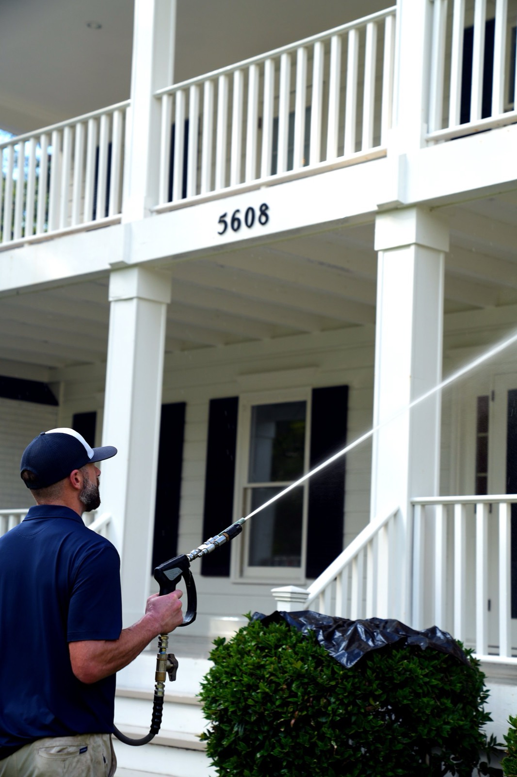Worker washing the columns and rails of a two-story porch on a white house