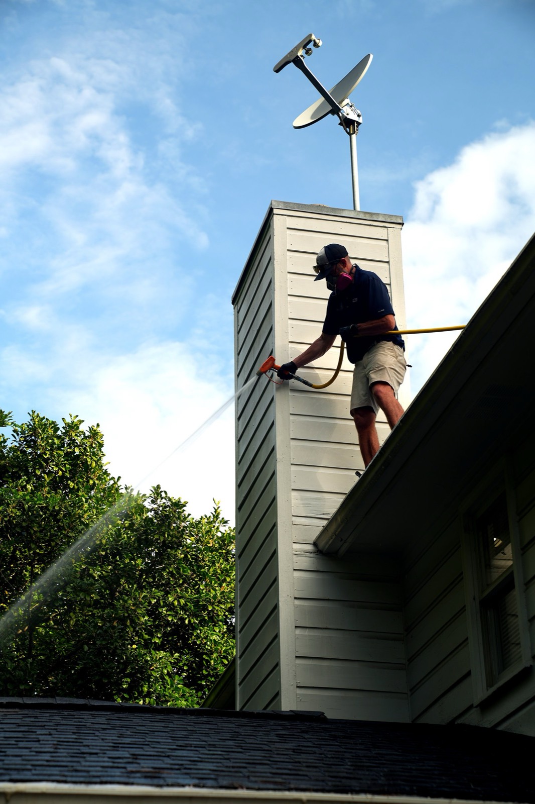 Worker soft washing a chimney and roofline from the roof of a house
