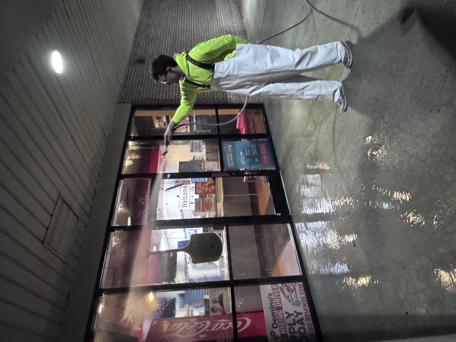 Worker in hi-vis washing a storefront window and walkway at night